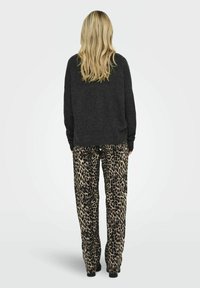 Tamno sivi oversized pulover s dugim rukavima, uparen s labavim hlačama s leopard printom koje imaju bež i crnu šaru. Ovaj outfit ima opušteni kroj.