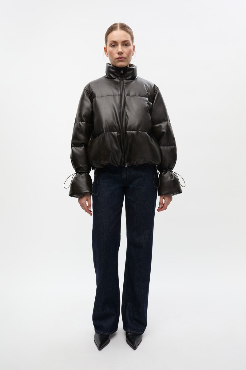 Geacă neagră puf cu guler înalt, închidere cu fermoar și manșete elastice. Purtați cu blugi evazați albastru închis și pantofi cu toc ascuțit negri.