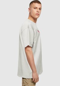 Kortærmet lys grå t-shirt lavet af bomuld, med et farverigt broderet design på forsiden, afslappet pasform og rund halsudskæring.