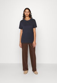 Camiseta de algodón azul marino de manga corta, con cuello redondo y un diseño sutil en el pecho, combinada con pantalones de pierna ancha marrones y zapatos claros.