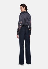 Silk blouse with patterned sleeves, paired with dark denim trousers. The trousers have a straight-leg design and are complemented by sneakers.