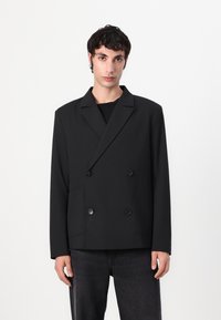 Doppelreiher schwarzer Blazer aus strukturiertem Stoff mit zwei Vorderfächern und großen Knöpfen. Gerader Schnitt mit Reverskragen.