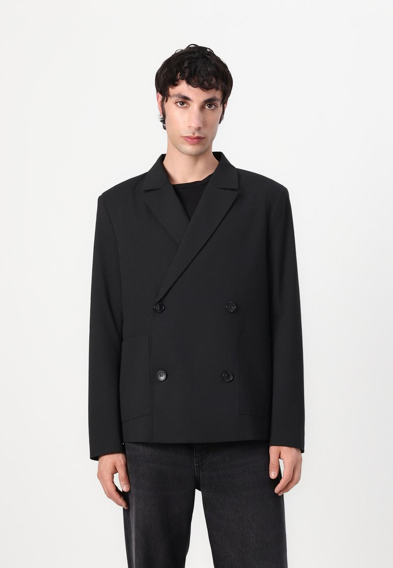 Doppelreiher schwarzer Blazer aus strukturiertem Stoff mit zwei Vorderfächern und großen Knöpfen. Gerader Schnitt mit Reverskragen.
