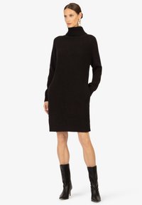 Schwarzes Strickkleid mit hohem Rollkragen, langen Ärmeln und seitlichen Taschen. Die Textur ist gerippt und sorgt für einen gemütlichen Look.