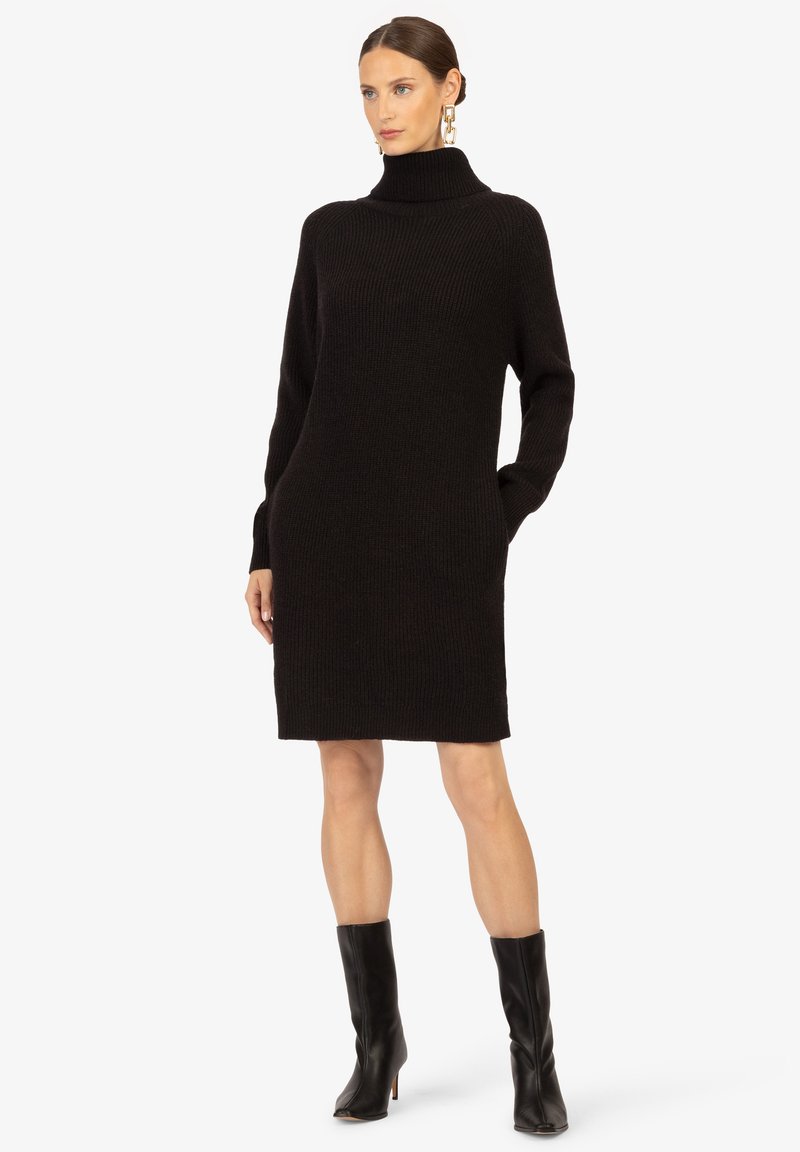 Schwarzes Strickkleid mit hohem Rollkragen, langen Ärmeln und seitlichen Taschen. Die Textur ist gerippt und sorgt für einen gemütlichen Look.
