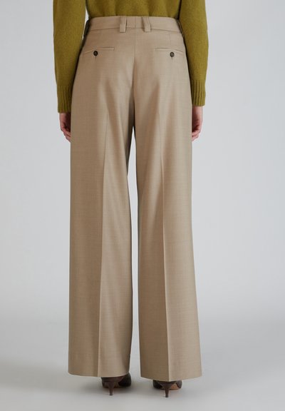 Beige wijde broek met een soepele textuur, voorzien van twee achterzakken met knopen. Gestyled met een groene trui en bruine hakken.