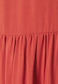 Koralfarbenes Midikleid aus einem glatten Stoff, mit einem gerafften Bund für zusätzliches Volumen. Das Material wirkt strapazierfähig und leicht.