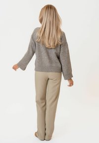 Szürke kötött pulóver laza szabással és széles ujjal, világos bézs nadrággal párosítva. Az anyag lágy, finom textúrával rendelkezik.