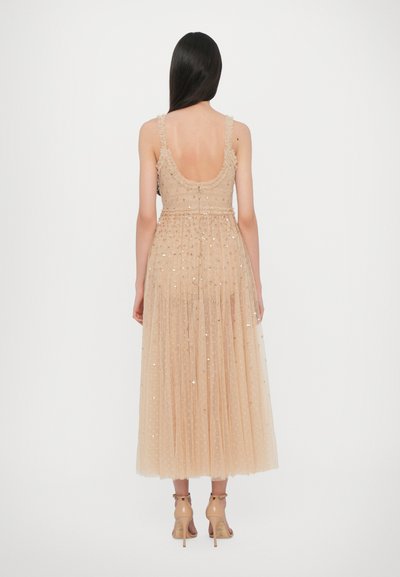 Abito in tulle nude con profondo scollo a V sul retro, spalline con volant e paillettes sparse. Pieghe fluenti che arrivano a metà polpaccio, abbinato a tacchi beige con cinghie.