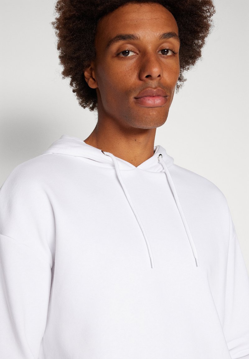 Felpa bianca con cappuccio regolabile, tessuto morbido e vestibilità comoda. Presenta un design minimalista senza motivi o loghi visibili.