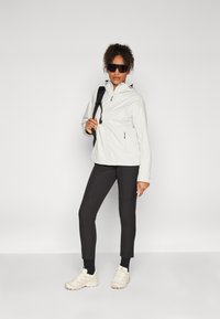 Lätt, vit zip-up jacka med huva, kombinerad med svarta, åtsittande byxor och beiga sneakers. Slät textur, minimalistisk design.