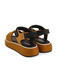 Sandalias de plataforma marrones con suela gruesa, parte superior texturizada y acentos negros. Correa ajustable con herrajes metálicos en el tobillo.
