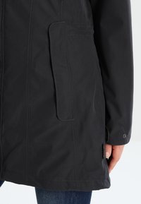 Veste noire imperméable avec une poche latérale, une texture lisse et une fermeture à pression au niveau du poignet, au design épuré et minimaliste.