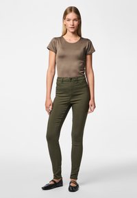 Olive green high-waisted jeans with a slim fit, paired with a fitted brown t-shirt. Black ballet flats complete the outfit.