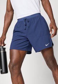 Ναυτικό μπλε σορτς τρεξίματος με ελαστική μέση και κορδόνι. Διαθέτει γκρι λογότυπο Nike στην κάτω αριστερή πλευρά. Μαλακή υφή.