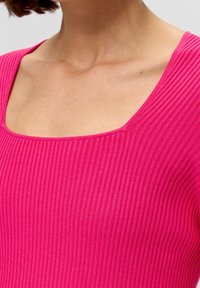 Aansluitende geribbelde top in felroze met een brede ronde hals. Het materiaal is textuurrijk en elastisch, waardoor de top goed aansluit rond de torso.