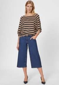 Gestreiftes beige und marineblaues Langarmoberteil, kombiniert mit weit geschnittenen blauen Denim-Culottes. Mit einem schwarzen Gürtel mit metallic Akzent.