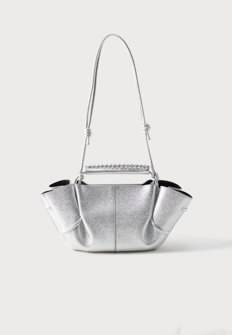 Ασημί τσάντα με υφή και χαλαρή φόρμα, δύο λεπτά λουράκια ώμου με κόμπους και μια τυλιγμένη λαβή στην κορυφή.