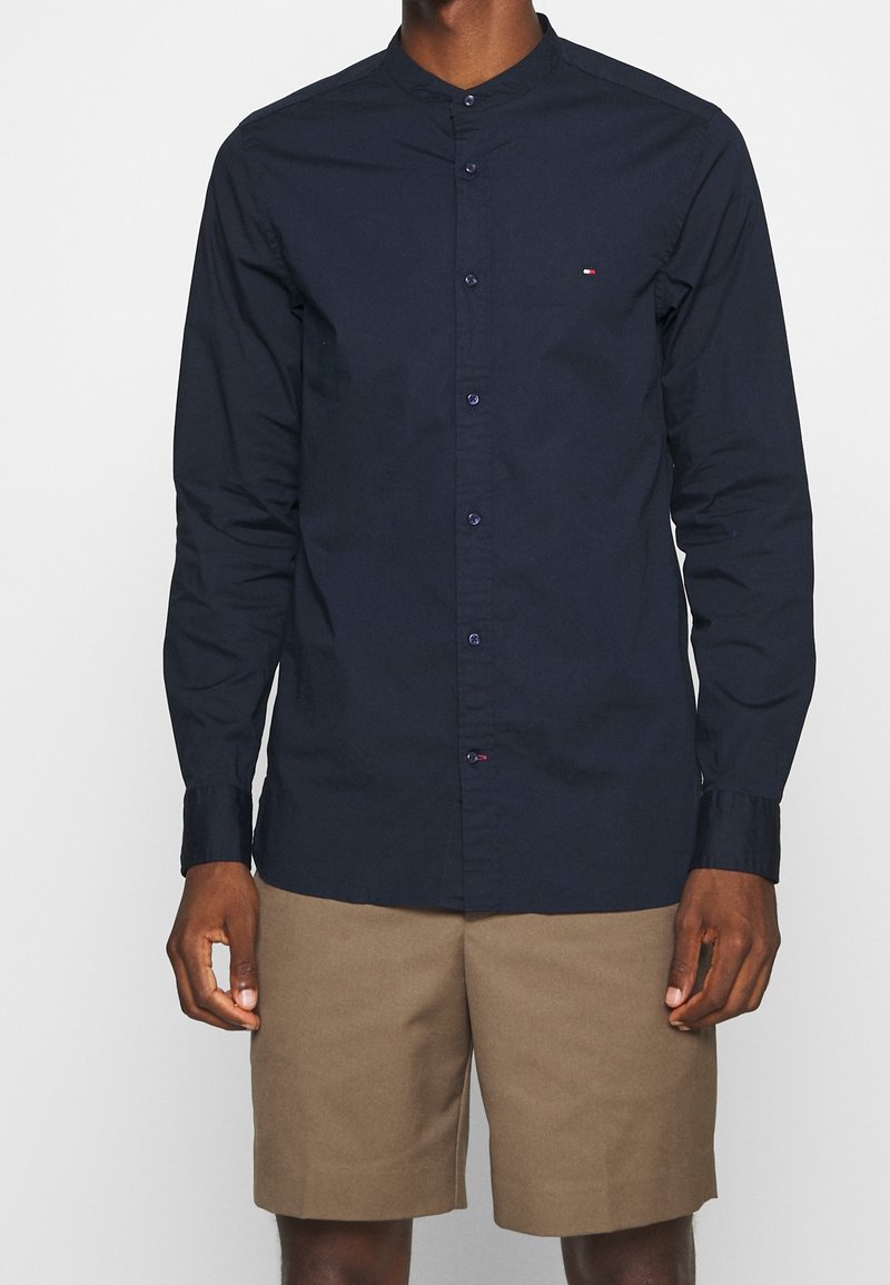 Maglietta a maniche lunghe blu navy con collo alla coreana, chiusura con bottoni e piccolo dettaglio logo sul petto. Tessuto in cotone liscio.