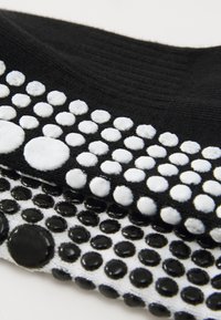 Calcetines en blanco y negro con puntos elevados de diferentes tamaños. El calcetín negro tiene puntos blancos, mientras que el calcetín blanco tiene puntos negros.