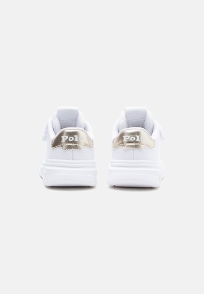 Zapatillas deportivas blancas con suelas gruesas, con lengüetas doradas en el talón con la marca "Polo", mostradas desde atrás sobre un fondo liso y claro.