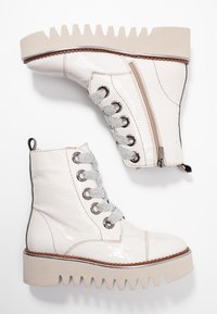 Valkoiset patenttinahkaiset nilkkurit, joissa on harmaat nauhat, vetoketju ja paksu beige uritettu pohja. Varustettu vahvistetuilla nauhojen reijillä ja kantalenkillä.