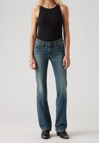 Dark blue denim flared jeans with a mid-rise waist, front pockets, and slight fading. Paired with a black ribbed tank top and black shoes.