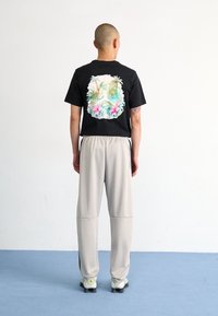 Svart t-shirt med en färgglad tropisk design på baksidan; matchad med ljusgrå, löst sittande byxor och svarta träningsskor.