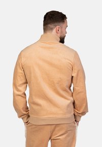Giacca in corduroy beige con colletto alto, texture a coste e polsini elasticizzati, caratterizzata da una vestibilità comoda e senza marchi visibili.