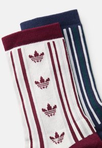 Pletené ponožky s bielym základom a víno červenými pruhmi a logom, spolu s námorníckou ponožkou s vertikálnymi zelenými a bielymi pruhmi.