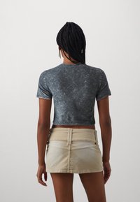 Cropped, short-sleeve top in a faded black fabric; paired with a light beige denim skirt featuring a back pocket and a waistband.