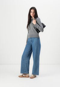 Gray long-sleeve top paired with wide-leg blue denim jeans and beige sneakers featuring a leopard pattern. Black bag slung over shoulder.