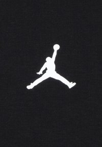 Tessuto nero con logo Jumpman bianco, che raffigura una figura che salta con un pallone da basket, evidenziando la trama liscia e il contrasto.