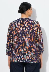 Bluse mit Blumenmuster in Dunkelpurpur mit orangefarbenen und grünen Akzenten, dreiviertelärmlig und in lockerer Passform. Glatte Textur des Stoffes.