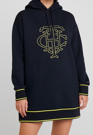 Robe sweat à capuche bleu marine avec un grand logo jaune, des poignets et un ourlet côtelés présentant des détails de couture contrastants jaunes. Manches longues avec une coupe ample.