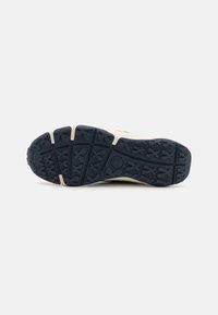 Navy rubber sneaker outsole with textured tread, featuring cross patterns and a logo, reinforced heel, and contrasting cream midsole.