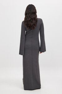 Robe en tricot grise longue avec des manches évasées, présentant un corsage ajusté et une silhouette droite, longueur traîne. Coutures le long du dos.