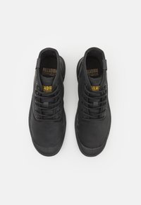 Scarpe sportive nere in tela con design con lacci, suole in gomma, colletto imbottito e un'etichetta in tessuto sulla linguetta. Texture liscia e forma aerodinamica.