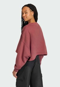 Felpa color vinaccia, oversize, tagliata, in tessuto misto cotone con spalle scese. Abbinata a pantaloni cargo neri con tasche.