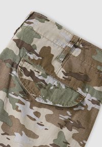 Section de tissu avec un motif camouflage vert, brun, beige et blanc et une poche à rabat avec des coutures visibles sur un fond clair.