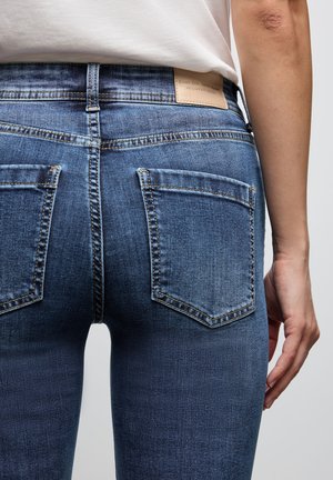 Donkerblauwe denim jeans met een aangesloten ontwerp, voorzien van twee achterzakken en een leren logopatch op de tailleband. Licht vervaagde textuur.