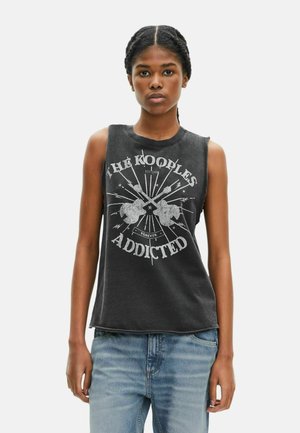 Camiseta sin mangas negra con estampado gráfico que dice "The Kooples Addicted". Presenta una textura suave y un ajuste relajado, con bordes sin rematar.