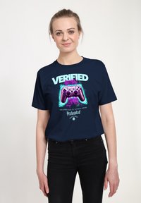 Camiseta de color azul marino con un gráfico de un controlador de juego morado y el texto "VERIFICADO" y "PRECARGADO". Manga corta, ajuste relajado.