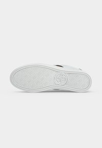 Semelle de sneaker blanche avec motif de grip texturé et logo circulaire embossé au centre sur fond blanc uni.