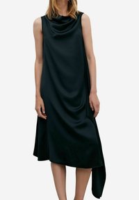 Robe noire sans manches en tissu lisse, avec un décolleté drapé et un ourlet asymétrique qui tombe plus long d'un côté.