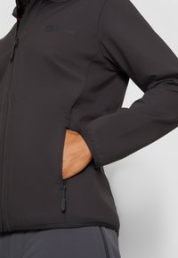 Zwarte softshell jas met een slim fit ontwerp, ritszakken en contraststiksels. Heeft een matte afwerking en een logo op de borst.