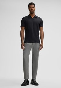 Black short-sleeve polo shirt with a collar, paired with light gray patterned trousers and black leather shoes.