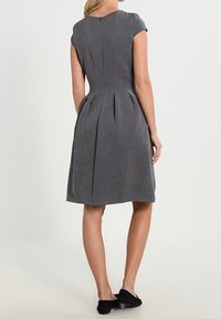Grå klänning med en skräddarsydd överdel, korta ärmar och plisserad kjol. Tillverkad av textilerad tyg med en diskret dragkedja i ryggen.