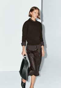 Maglione di lana marrone, camicia scura sotto, gonna di pelle marrone, borsa nera con hardware argento, stivali neri alla caviglia, design minimalista.