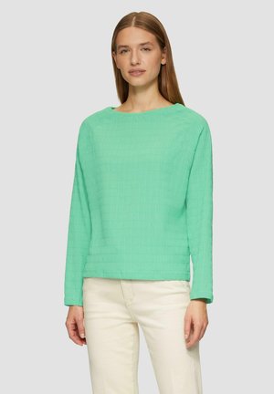 Haut vert menthe à manches longues avec un motif de grille texturé, encolure ronde et coupe décontractée, associé à un pantalon de couleur claire.